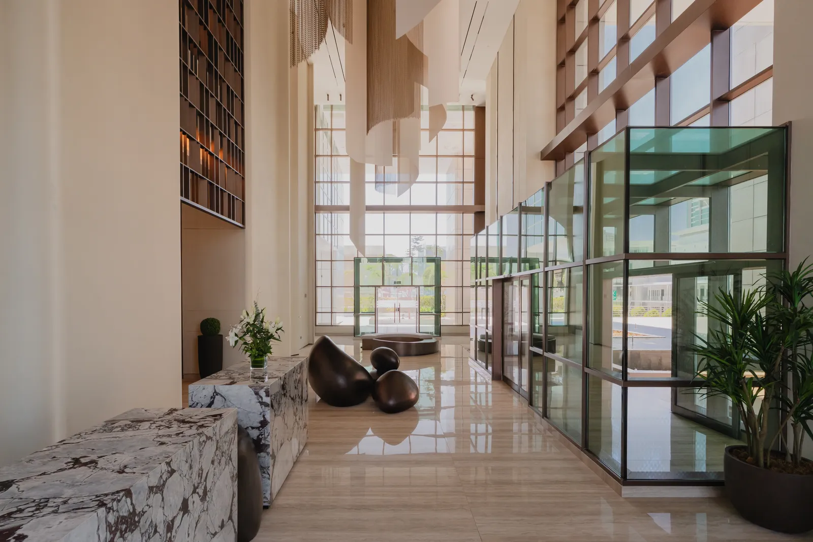 The lobby: marble-faced reception counters, the bronze pebble sculpture, a tall glazed entrance with green-tinted glass vestibules, and sheets of fabric hanging in the double-height space