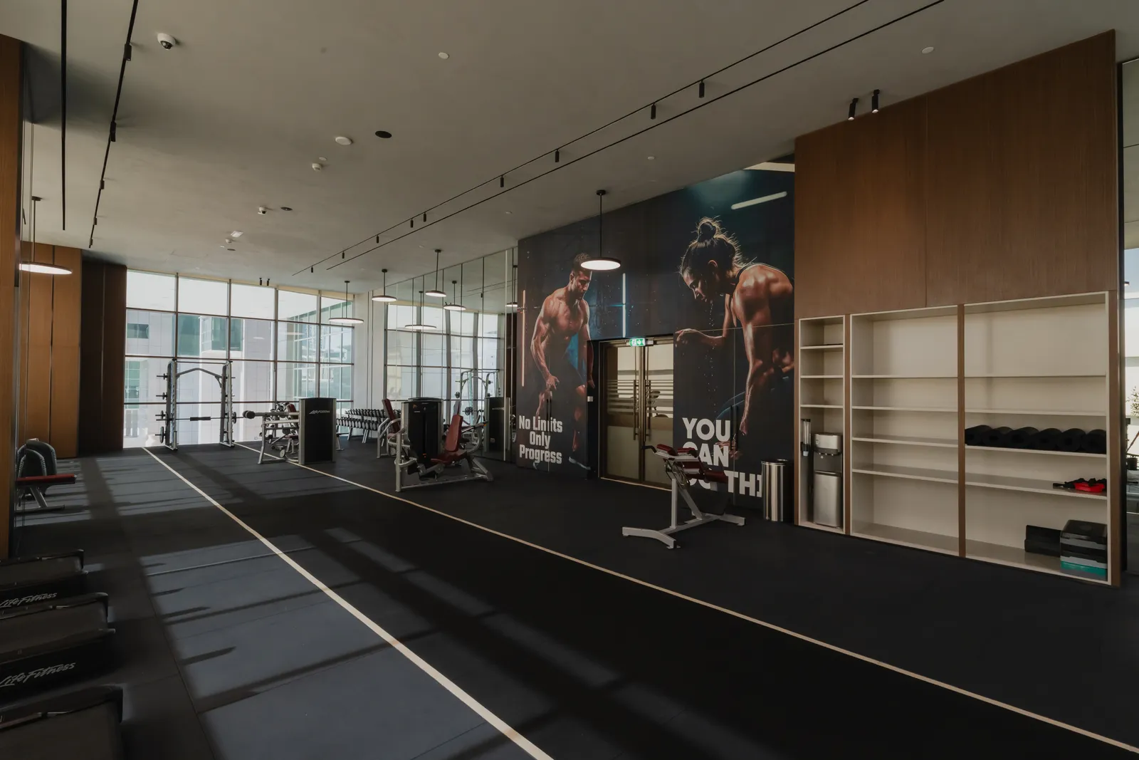 The gym: strength machines, a Smith machine, two motivational posters, a timber shelving wall with kettlebells and a water cooler