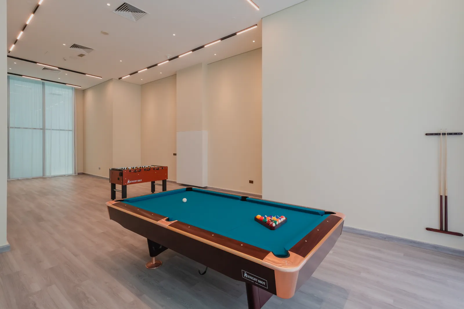 The games room: the billiards table with the balls racked, table football behind, cues on the wall and tall windows