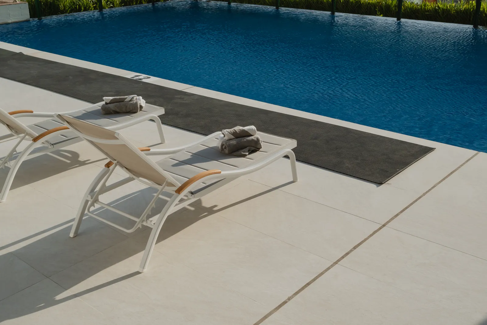 Two loungers with rolled towels at the pool's edge, a black drainage mat along the coping and a depth marking of 1.2