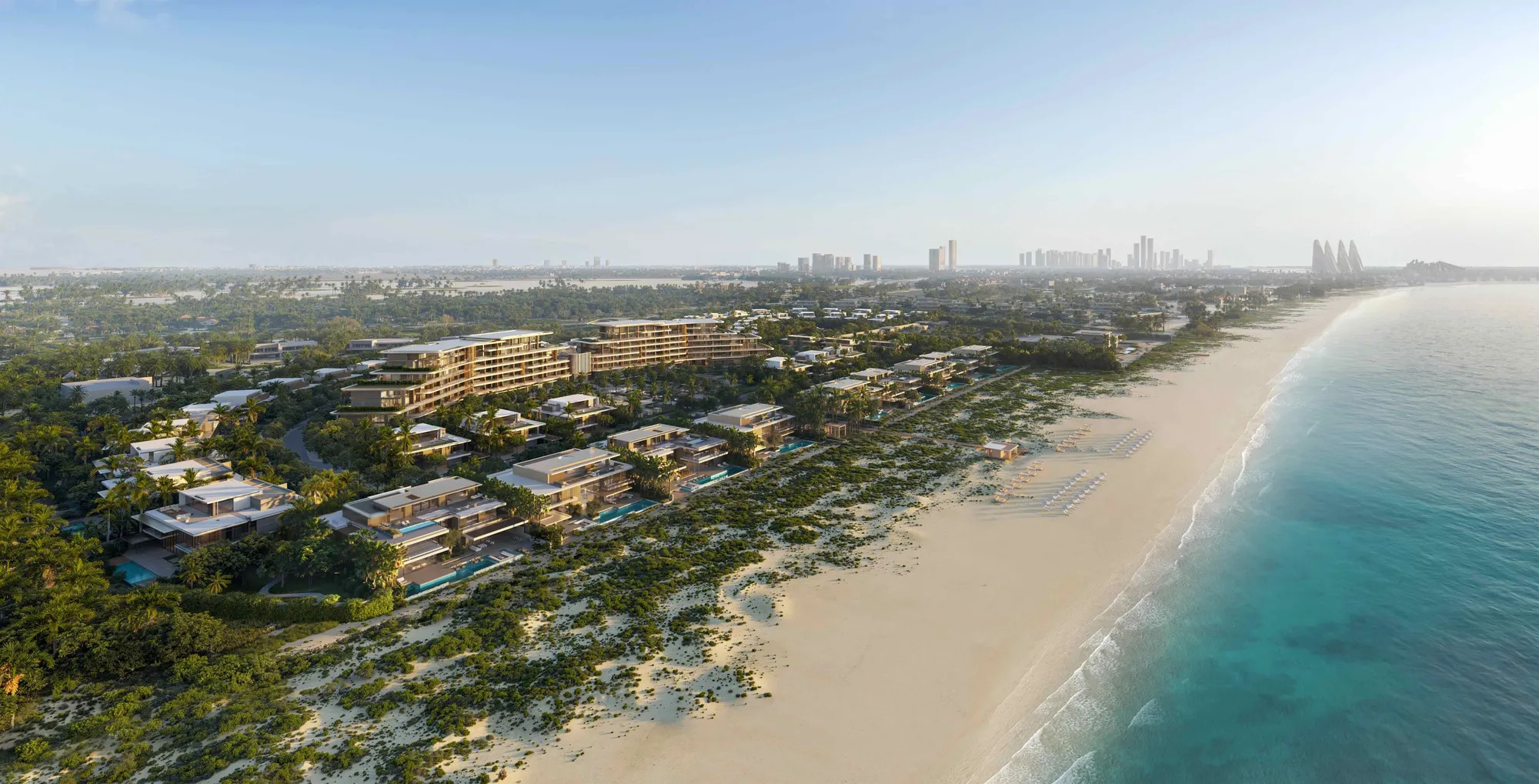 The estate along Saadiyat Beach from the air: the villa arcs and the curved suites building behind the beach, the sea to the left and the Abu Dhabi skyline on the horizon