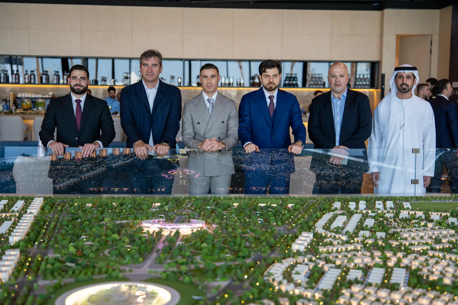 Six men in suits and kandura standing behind the scale model, the circular park and its lit landmark in the model’s centre