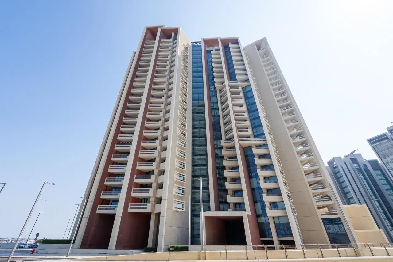 Marafid Tower from the street, looking up against a blue sky: three cream-and-terracotta sections of balconies around a dark glazed core, with retail glazing at street level