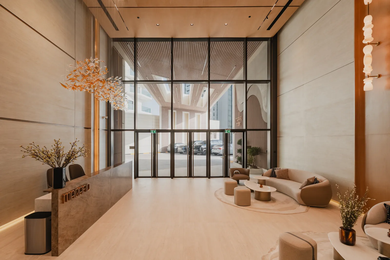 The lobby looking towards the glazed entrance: a seating group of cream armchairs and stools, dried flowers on a side table, bronze lift portal to the right