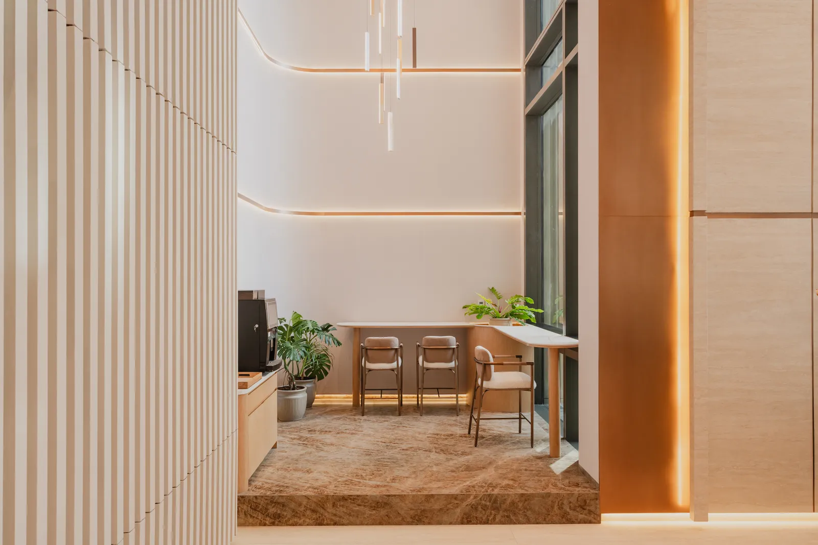 The coffee corner from the fluted-wall side: the counter and machine, tables and chairs, planting and the pendant cascade above