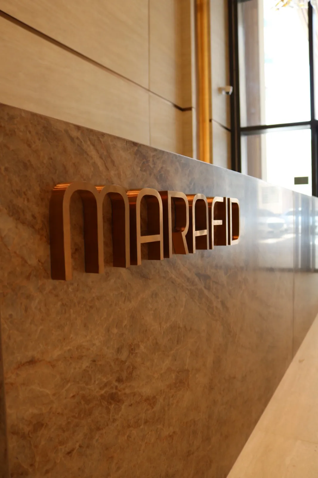 The bronze MARAFID wordmark on the brown marble reception desk, close up